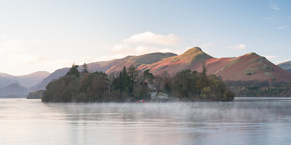 Derwent Isle is reflected in a calm misty Derwentwater infront of Catbells at sunrise during Autumn.