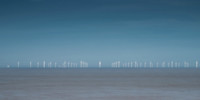 Many wind turbines out at sea in the distance on the horizon.