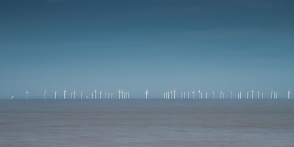 Many wind turbines out at sea in the distance on the horizon.
