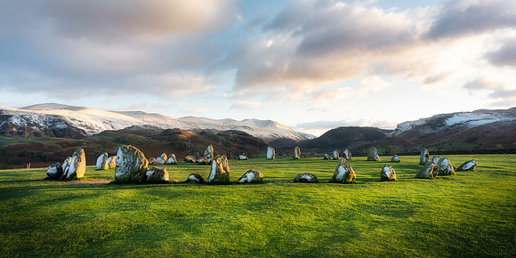 Sunset at Castlerigg Stone Circle with snow covered mountains and long shadows.