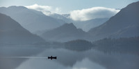 A man sails across Derwentwater lake in a canoe at sunrise with mist on the water.