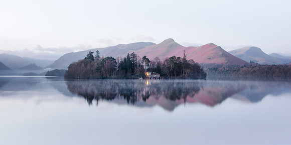 Derwent Isle is reflected in a calm misty Derwentwater infront of Catbells before sunrise during late winter.