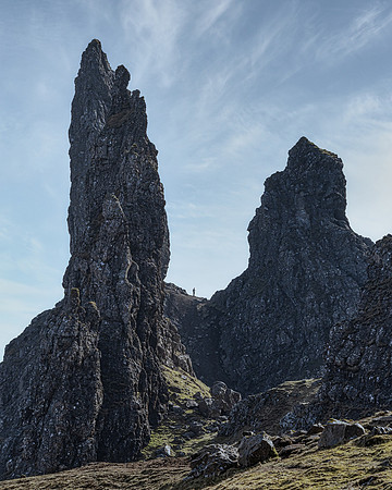 A man appears very small standing at the base of the Old Man of Storr pinnacles on Isle of Skye.