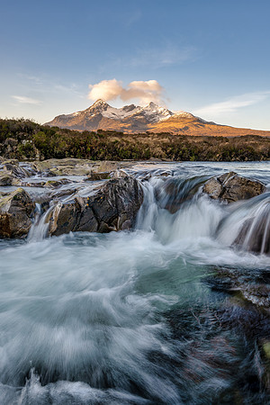 Water crashes over a waterfall with the snow covered mountains of the Cuillin at Sligachan on the Isle of Skye.