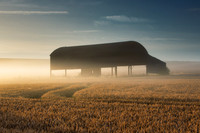 Dutch barn in a field of wheat is lit up by the rising golden sun through a low mist at Sixpenny Handley.