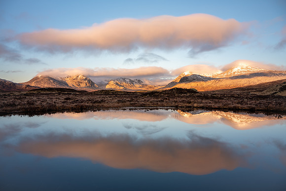 Sunrise lights up the snow covered Black Mountains reflected in the lochen on Rannoch Moor in Scotland.