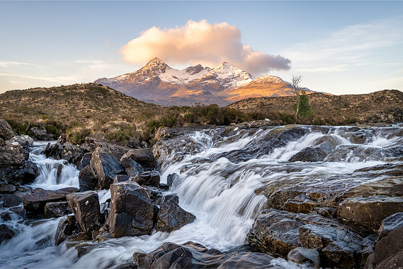 Water crashes over a waterfall with the snow covered mountains of the Cuillin at Sligachan on the Isle of Skye.